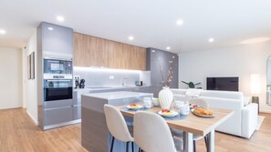 Une cuisine moderne dotée d’un four encastré, un coin repas avec une table mise pour le petit-déjeuner, et un salon avec un canapé et une télévision.