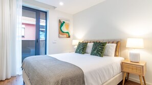 Ein Hotelzimmer mit einem Bett, zwei Nachttischlampen, einem Wandbild und Blick durch eine Tür.