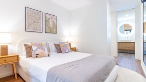 A hotel bedroom with a large bed, two bedside tables, a nightstand, a wall-mounted lamp, and two framed artworks above the bed. - Polacos Residence | 2BR | Apt O by LovelyStay (Vila Nova de Gaia)