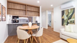 Eine moderne Küche mit Holzausbau, ein Essbereich mit rundem Tisch und Stühlen sowie ein Wohnzimmer mit weißem Sofa.