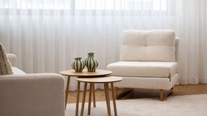 Ein Zimmer mit einem weißen Sessel, einem runden Holztisch mit zwei gestreiften Vasen und einem weißen Sofa.