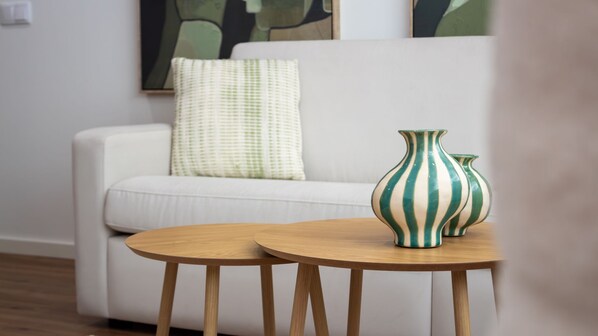 Ein Wohnzimmer mit einem weißen Sofa, einem runden Holztisch und zwei gestreiften Vasen.