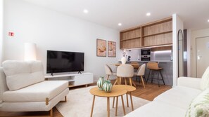 Ein modernes Wohnzimmer mit Flachbildfernseher, einer Couch, einem Couchtisch und einem Essbereich mit Stühlen.