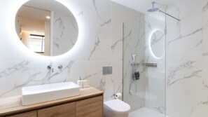 Een moderne badkamer met een grote spiegel, een rechthoekig wastafelmeubel, een toilet en een douchecabine met glazen wanden.