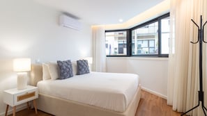 A hotel room with a bed, a bedside table with a lamp, a window with curtains, and an air conditioning unit. - Polacos Residence | 1BR | Apt C by LovelyStay (Vila Nova de Gaia)