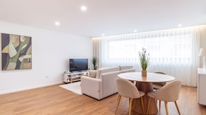 A modern living room with a sofa, a TV, a dining table with chairs, and a large window with curtains. - Polacos Residence | 1BR | Apt C by LovelyStay (Vila Nova de Gaia)