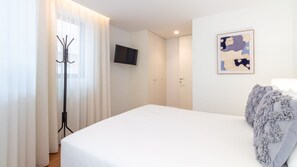 Quarto de hotel com cama, televisão, guarda-roupa e pintura abstrata emoldurada.