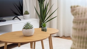 A round wooden table with two potted plants, a flat-screen TV, and a white sofa in a living room. - Polacos Residence | 1BR | Apt C by LovelyStay (Vila Nova de Gaia)