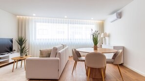 Uma sala de estar moderna com sofá, mesa de jantar com cadeiras, TV e planta.