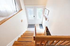 A staircase leading to a door with a glass panel, a small bench, and a wall-mounted light fixture. - Spacious 4BR House|15 Min to DT|DIX30|3 Parking| Central AC (Brossard)