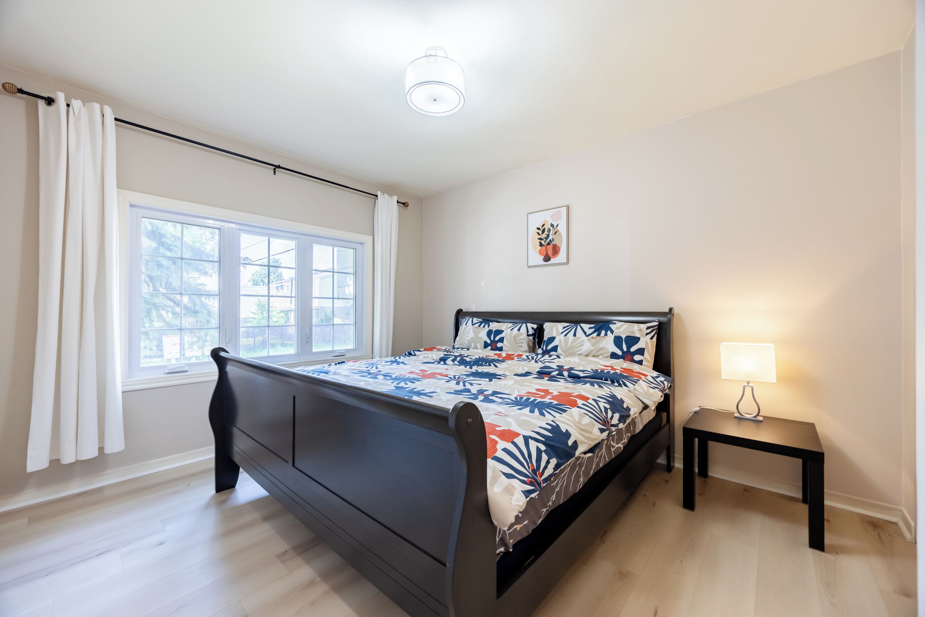 Un dormitorio con cama, ventana, mesita de noche y lámpara de pared.