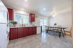 A modern kitchen with red cabinets, a white countertop, and a dining area with a table and chairs. - Spacious 4BR House|15 Min to DT|DIX30|3 Parking| Central AC (Brossard)