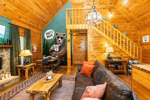 Een knus blokhut interieur met een eethoek, een bank, een open haard en een trap.