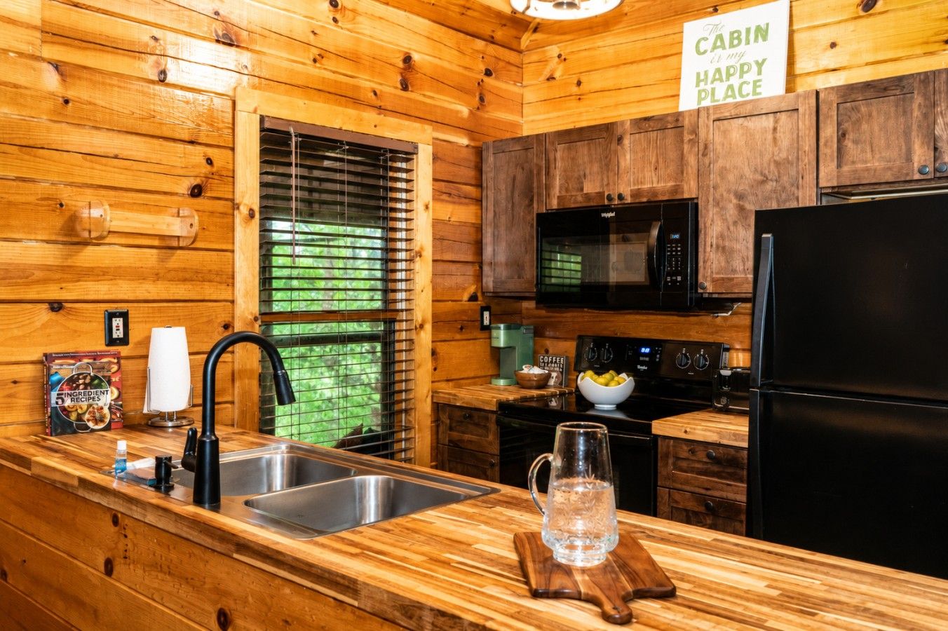 Una cucina in baita con pareti in legno, un lavello in acciaio inossidabile, un frigorifero nero e un forno a microonde.