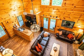 Ein Blockhaus-Interieur mit Holzvertäfelung, Kamin, Essbereich und einer Sitzecke mit Sofa und Couchtisch.