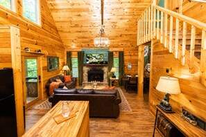 Ein Interieur einer Holzhütte mit Kamin, Holzwänden, einer Couch, einem Essbereich und einer Treppe.