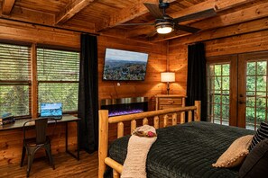 Une chambre dans un chalet en rondins, avec un lit, un bureau doté d’un ordinateur portable, une cheminée et un téléviseur fixé au mur.