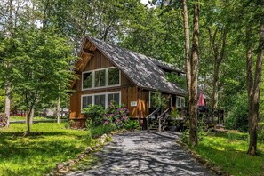 A wooden cabin with a gravel path leading to it, surrounded by trees and greenery.