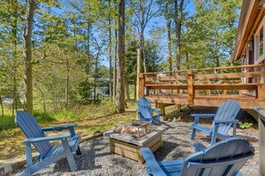An outdoor seating area with Adirondack chairs, a fire pit, and a wooden deck overlooking a forested area. - Chic A-Frame Cabin for a dreamy Poconos Escape (Tobyhanna)
