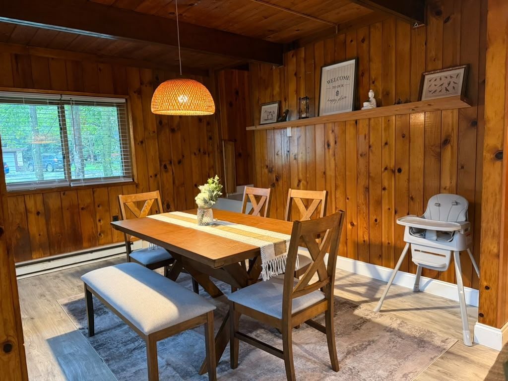 Ein Holzinterieur mit einem Esstisch, Stühlen, einer Bank, einem hochaufliegenden Baby-Stuhl und einer Pendelleuchte.