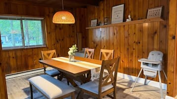 Ein Holzinterieur mit einem Esstisch, Stühlen, einer Bank, einem hochaufliegenden Baby-Stuhl und einer Pendelleuchte.