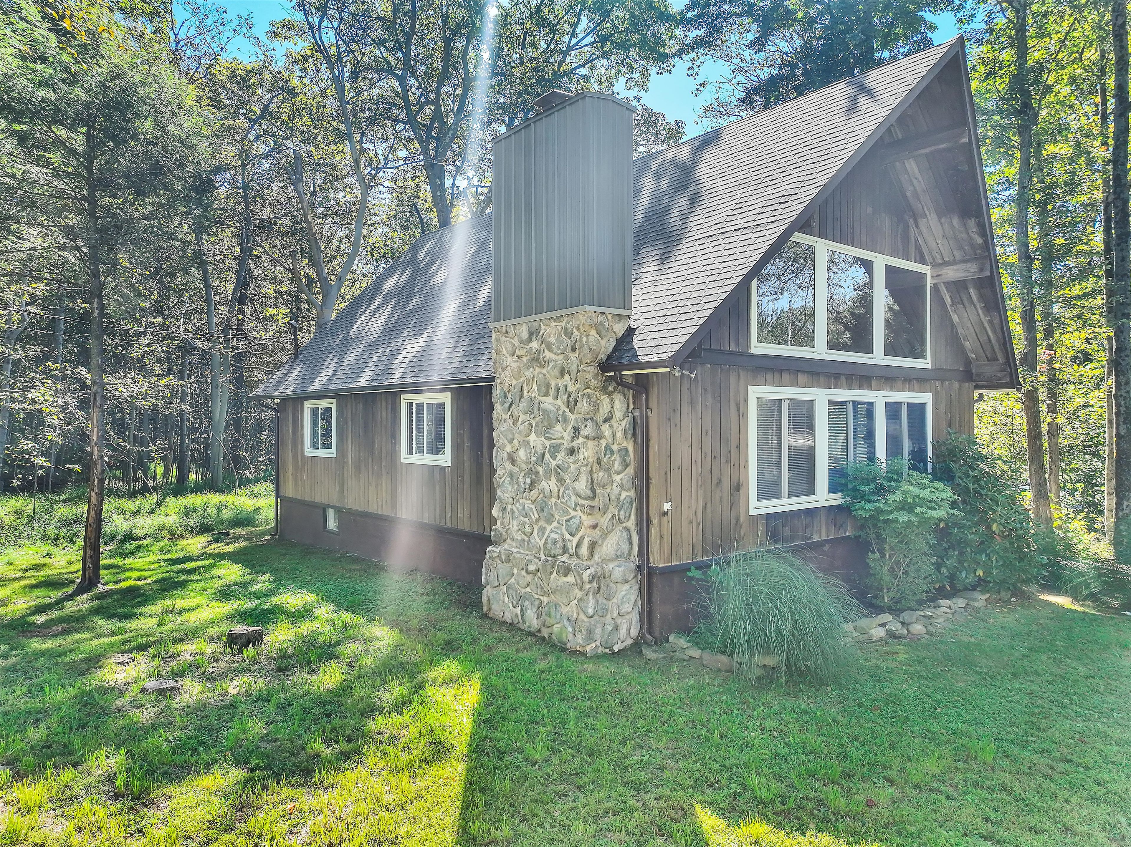 A two-story wooden house with a stone foundation, surrounded by a forested area.