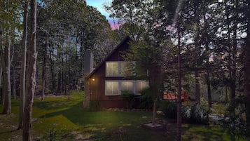 Eine Holzhütte mit Steinunterbau, großen Fenstern und einer Holzfassade, umgeben von einem bewaldeten Gebiet.