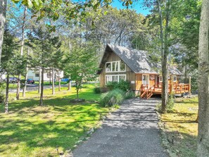 A wooden cabin with a gravel path leading to it, surrounded by trees and a grassy area.