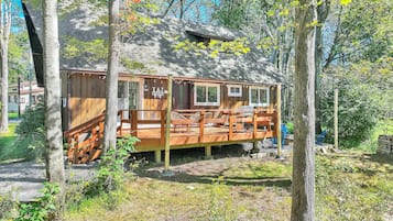 A wooden cabin with a deck, surrounded by trees.