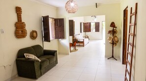 A living room with a sofa, a wooden guitar decoration, a wall-mounted hat rack, and a bed in the background.
