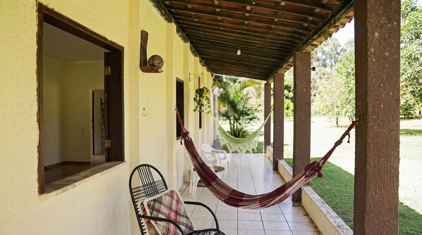 Un espacio al aire libre techado con una hamaca, sillas y vistas a un jardín.