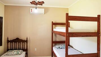 Una habitación con una litera, una cama individual con un cojín estampado, un cabecero de madera y un ventilador de techo.