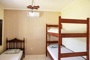 Una habitación con una litera, una cama individual con un cojín estampado, un cabecero de madera y un ventilador de techo.