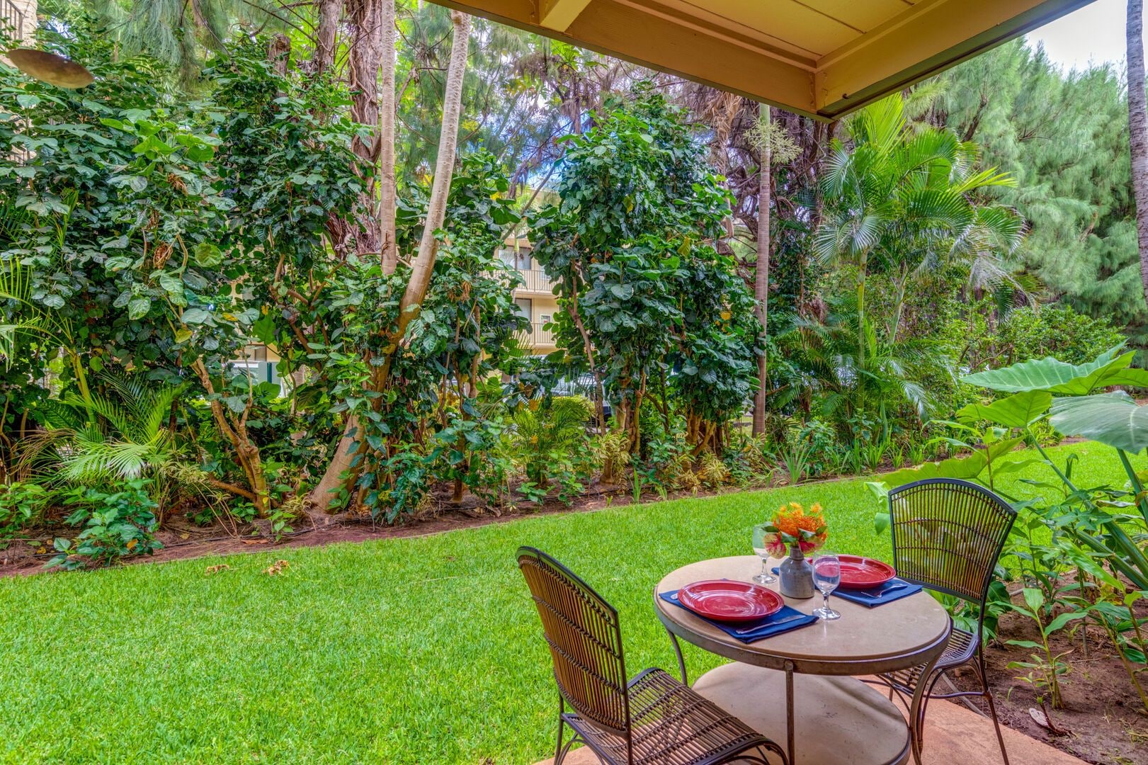 An outdoor patio with a table set for two, surrounded by lush greenery and trees.