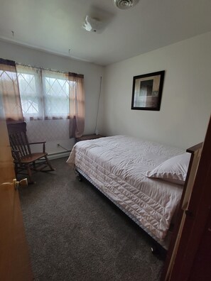 A bedroom with a single bed, a rocking chair, a framed picture on the wall, and a window with curtains. - The Plymouth Retreat 3 bedroom home  in the heart of PA Wilds  (Saint Marys)