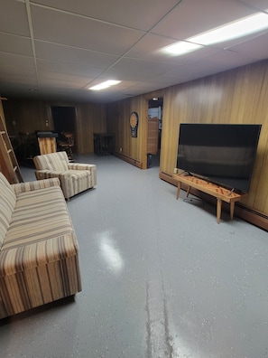 Una habitación con una televisión de pantalla plana sobre un soporte de madera, un dardo en la pared y sofás a rayas.
