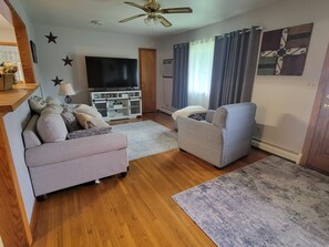 A living room with a sofa, armchair, TV, and decorative wall art. - The Plymouth Retreat 3 bedroom home  in the heart of PA Wilds  (Saint Marys)