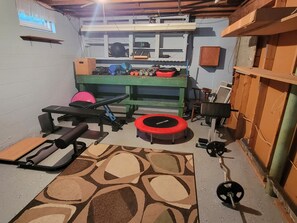 Un gimnasio en casa con equipo de ejercicio, una alfombra estampada y un banco verde.