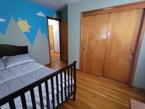 Un dormitorio con cama, suelo de madera, un armario y una pared con diseño de montaña y sol.