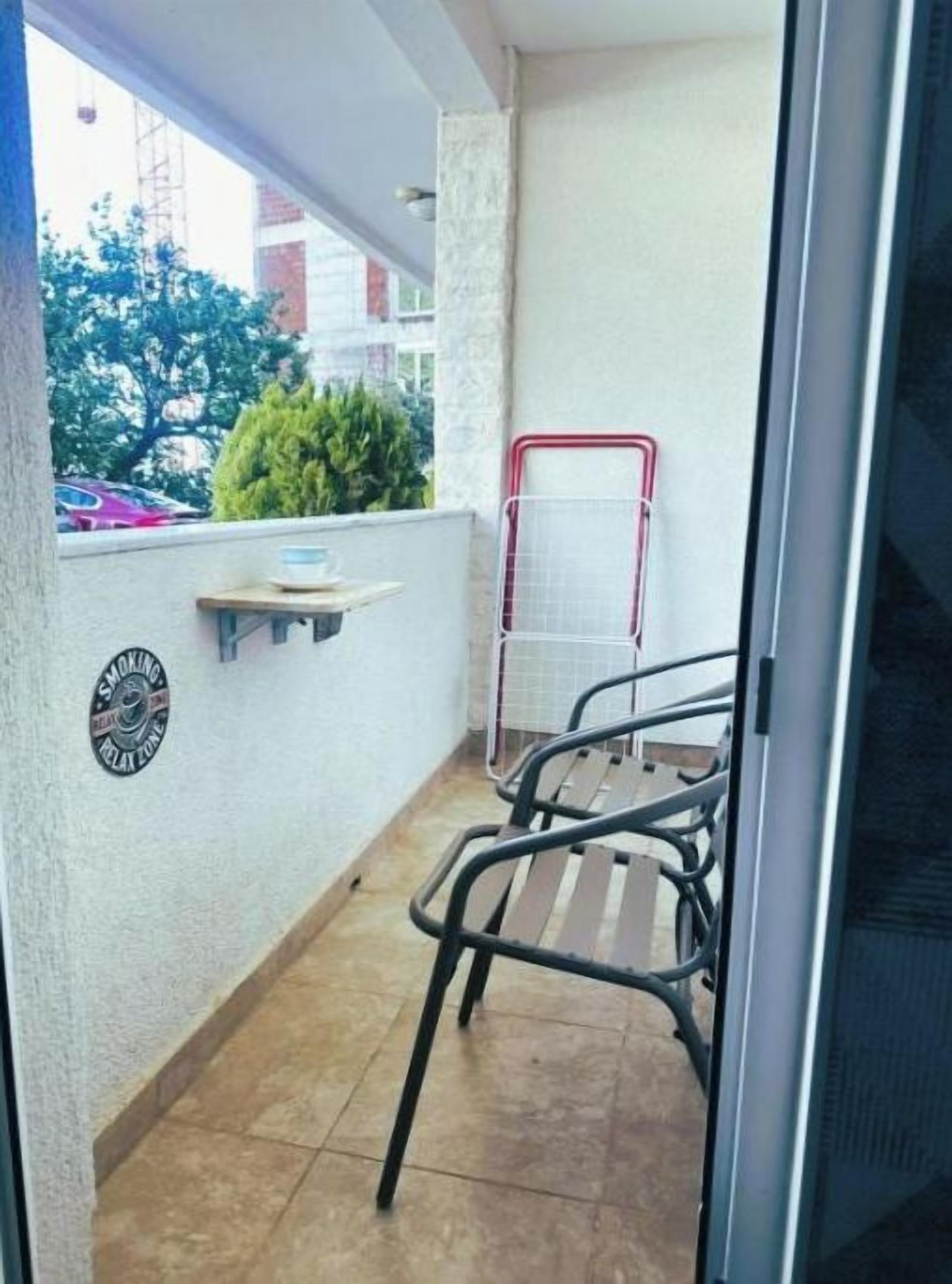 A balcony with a metal chair, a red metal rack, and a small table with a bowl.