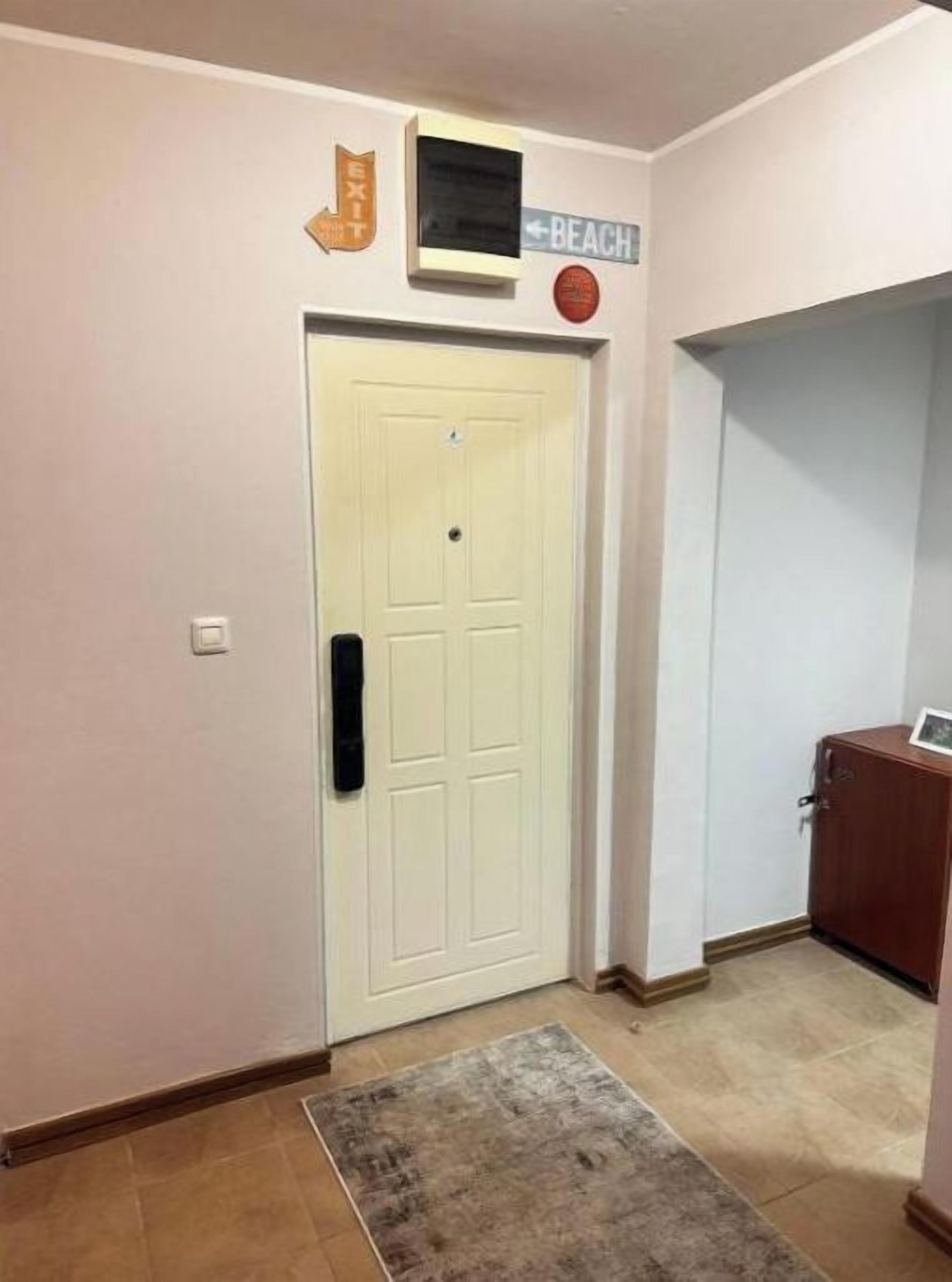 A hallway with a white door, a small screen above it, and a sign indicating 'BEACH' to the left.