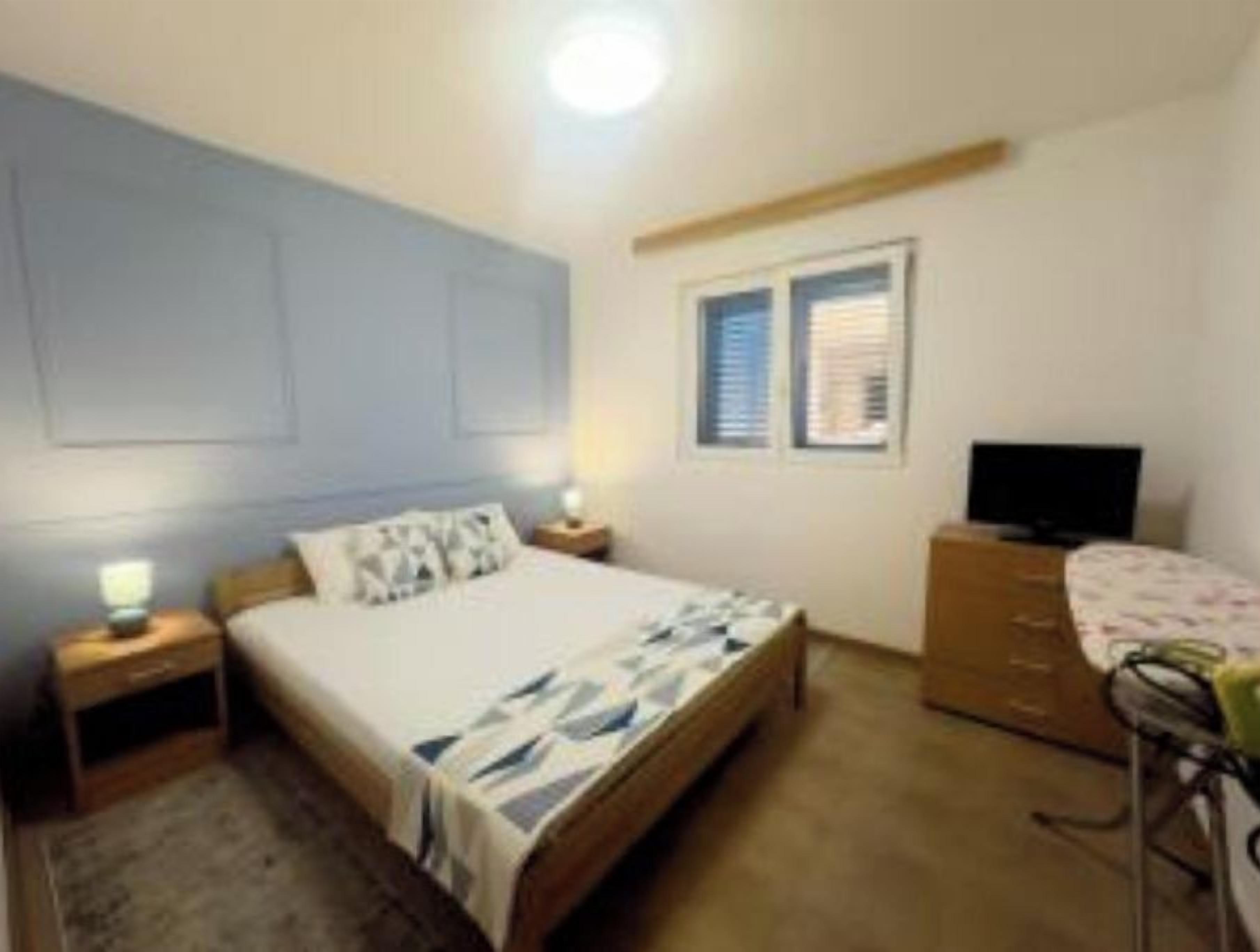 A bedroom with a bed, bedside table, lamp, dresser, and a television.