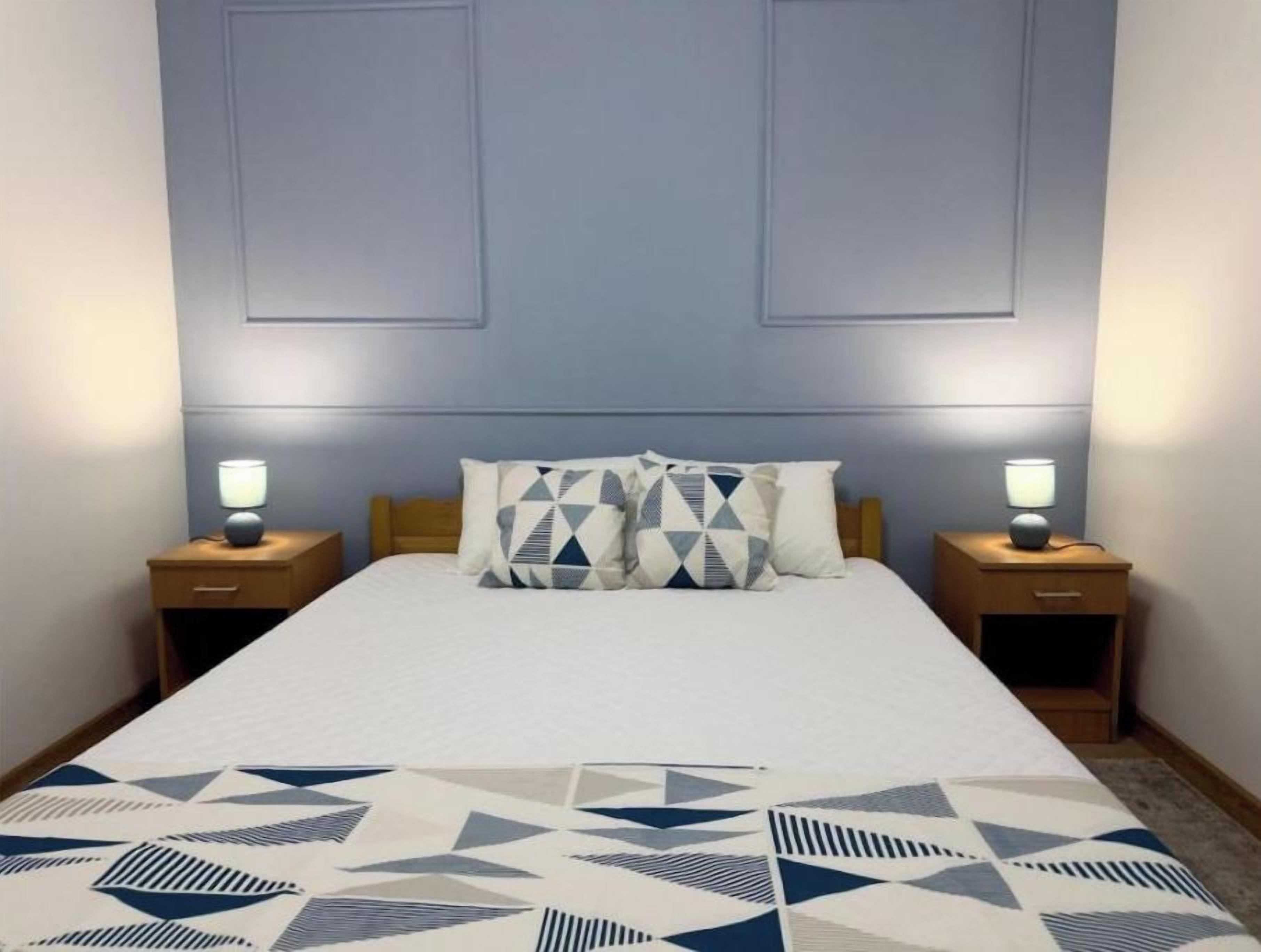 Una habitación de hotel con una cama grande, dos mesitas de noche y una colcha con estampado geométrico.