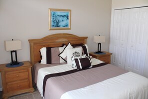 A neatly made bed with a headboard, two bedside tables with lamps, a wooden nightstand, a door, and a framed picture on the wall. - RC327- Family Retreat: 5BR with Pool & Games Room (DAVENPORT)