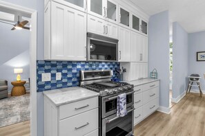 Een keuken met witte kastjes, een magnetron, een fornuis en een betegelde spatwand.