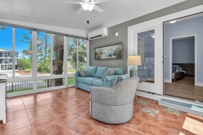A spacious living area with a large sliding glass door leading to a balcony, a grey armchair, a light blue sofa, and a painting on the wall. - Blue Lagoon: Gorgeous Home Near Waterway with Private Pool (Oak Island)