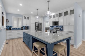 A modern kitchen with a central island, stainless steel appliances, and a blue and white color scheme. - Blue Lagoon: Gorgeous Home Near Waterway with Private Pool (Oak Island)