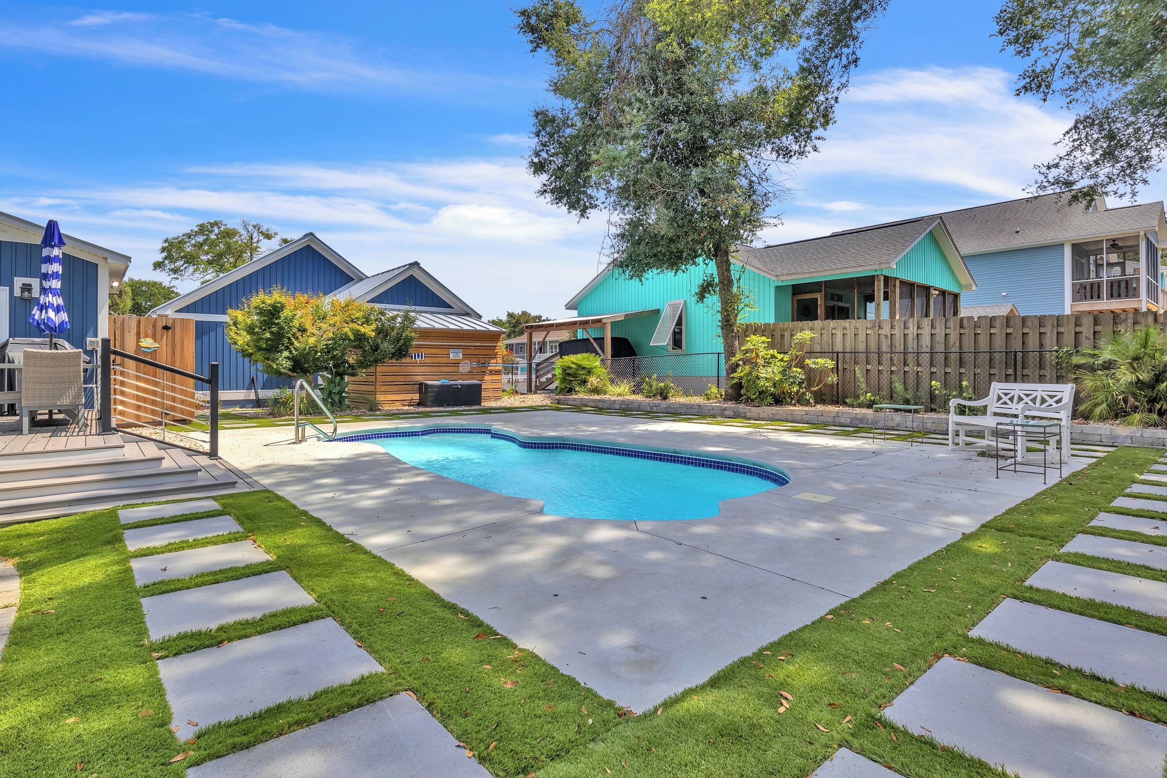 A backyard with a swimming pool, a wooden deck, and a fenced area.