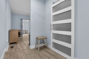 A hallway with a wooden cabinet, a stool, and a white door with frosted glass panels. - Blue Lagoon: Gorgeous Home Near Waterway with Private Pool (Oak Island)