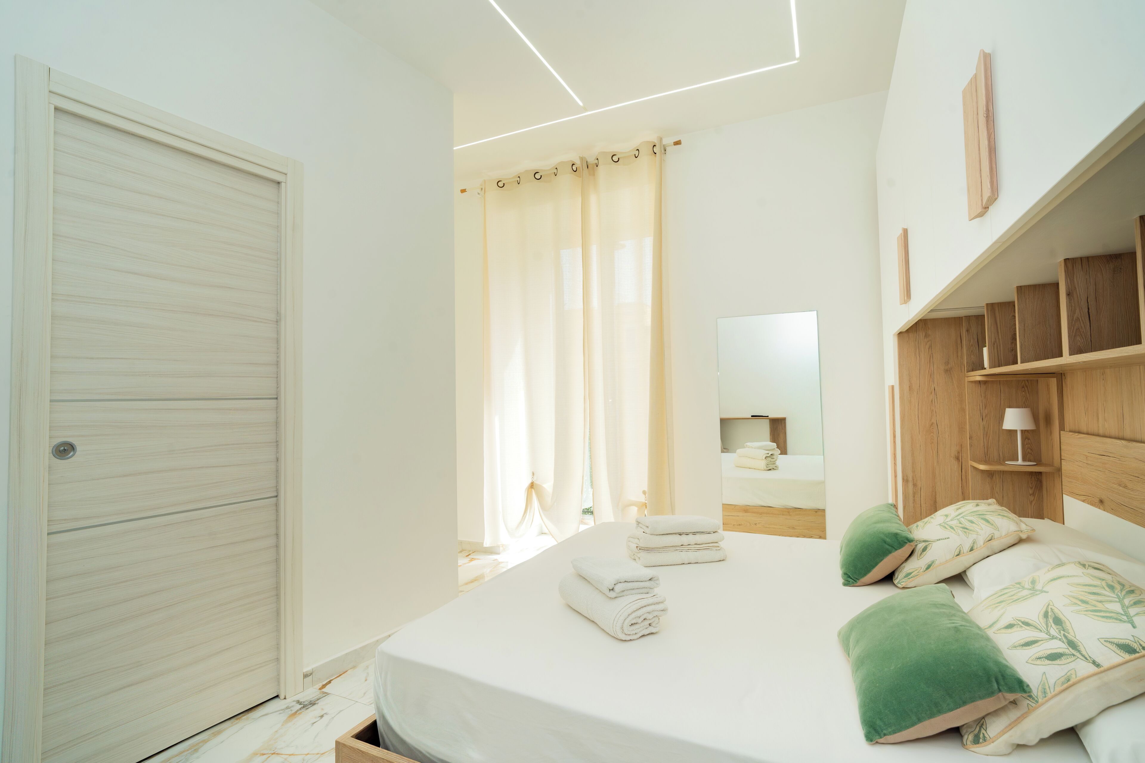 Ein Schlafzimmer mit einem Bett, einem Holzkopfteil, einem Nachttisch, einem Spiegel und einem Fenster mit Vorhängen.